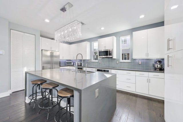 kitchen featuring sink, pendant lighting, a kitchen island with sink, white cabinets, and appliances with stainless steel finishes