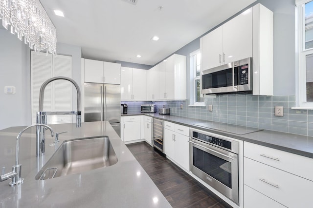 kitchen featuring backsplash, sink, appliances with stainless steel finishes, white cabinetry, and a chandelier