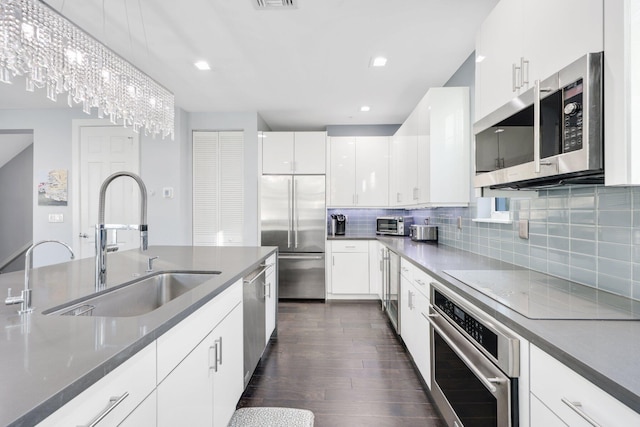 kitchen featuring sink, tasteful backsplash, white cabinetry, stainless steel appliances, and a chandelier