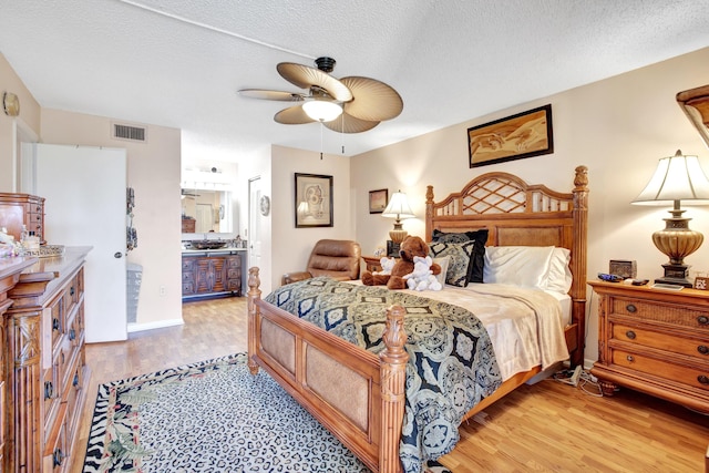 bedroom featuring a textured ceiling, ceiling fan, light hardwood / wood-style flooring, and ensuite bath