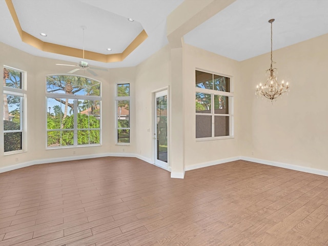 interior space with ceiling fan with notable chandelier, a tray ceiling, and light hardwood / wood-style flooring