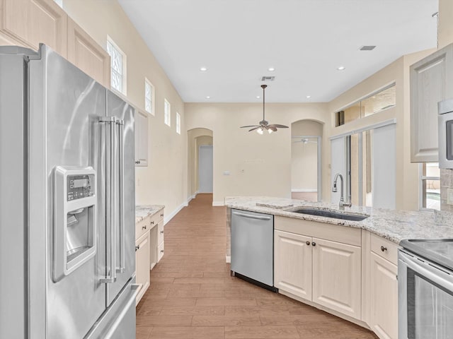 kitchen with sink, ceiling fan, light wood-type flooring, light stone counters, and stainless steel appliances