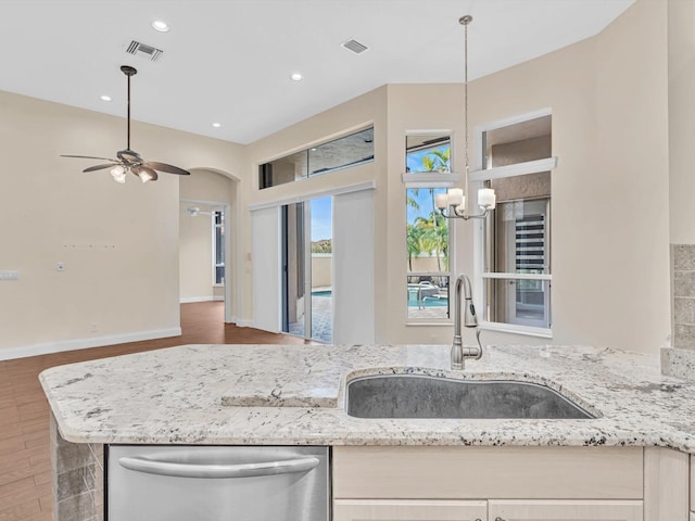 kitchen with pendant lighting, dishwasher, ceiling fan with notable chandelier, sink, and light stone countertops