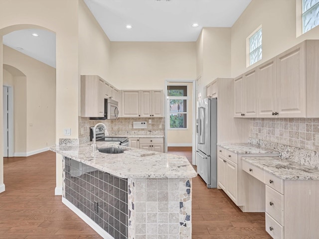 kitchen with light stone counters, light wood-type flooring, kitchen peninsula, stainless steel appliances, and a high ceiling