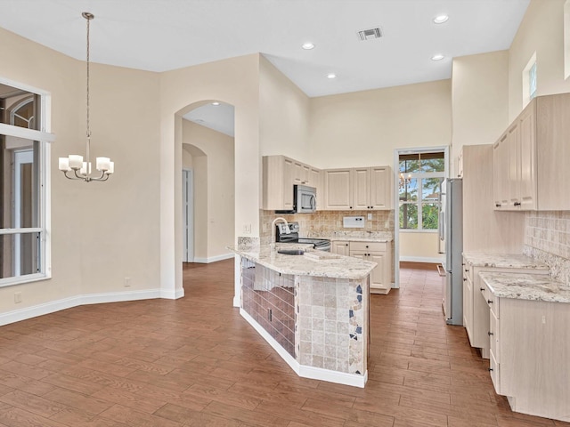 kitchen featuring pendant lighting, tasteful backsplash, hardwood / wood-style flooring, stainless steel appliances, and light stone countertops