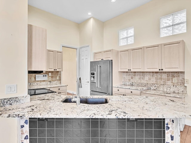 kitchen with sink, a towering ceiling, high quality fridge, light stone counters, and kitchen peninsula