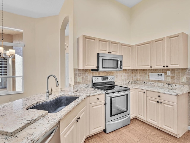 kitchen featuring pendant lighting, sink, light hardwood / wood-style flooring, light stone countertops, and stainless steel appliances