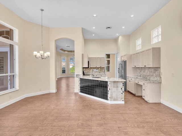 kitchen featuring sink, hanging light fixtures, tasteful backsplash, light stone counters, and light hardwood / wood-style flooring