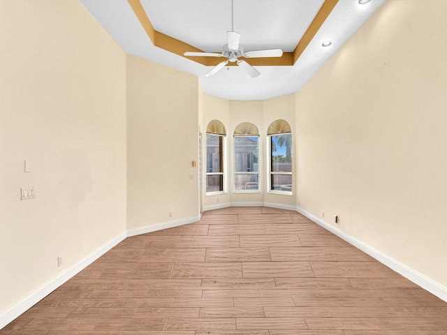 unfurnished room featuring ceiling fan, light wood-type flooring, and a tray ceiling