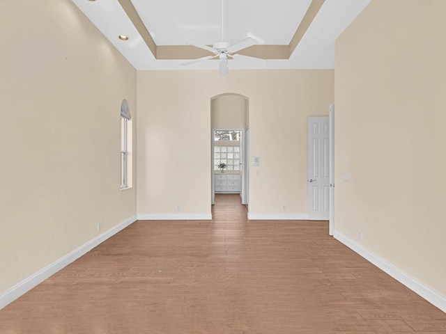 empty room featuring a raised ceiling, a healthy amount of sunlight, ceiling fan, and light hardwood / wood-style flooring