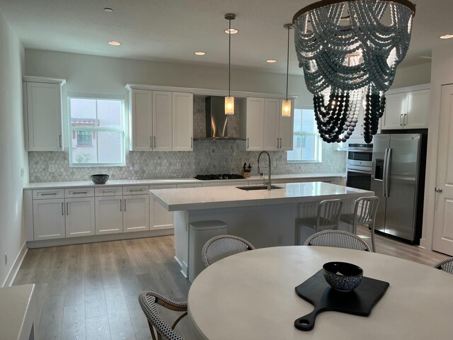 kitchen with appliances with stainless steel finishes, decorative light fixtures, white cabinetry, sink, and wall chimney exhaust hood