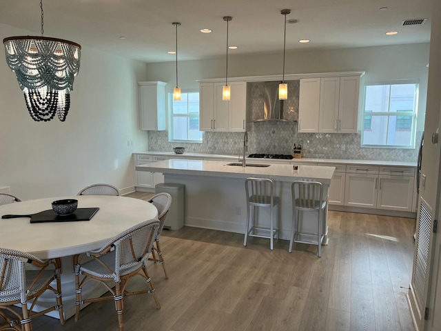 kitchen featuring white cabinets, decorative light fixtures, a breakfast bar, and wall chimney range hood