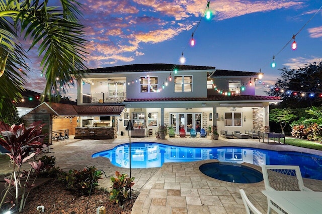 back house at dusk with a pool with hot tub, ceiling fan, a balcony, area for grilling, and a patio