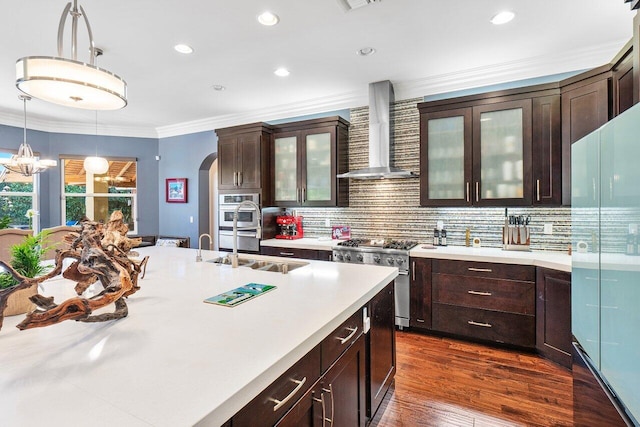 kitchen with appliances with stainless steel finishes, tasteful backsplash, wall chimney exhaust hood, dark brown cabinetry, and hanging light fixtures