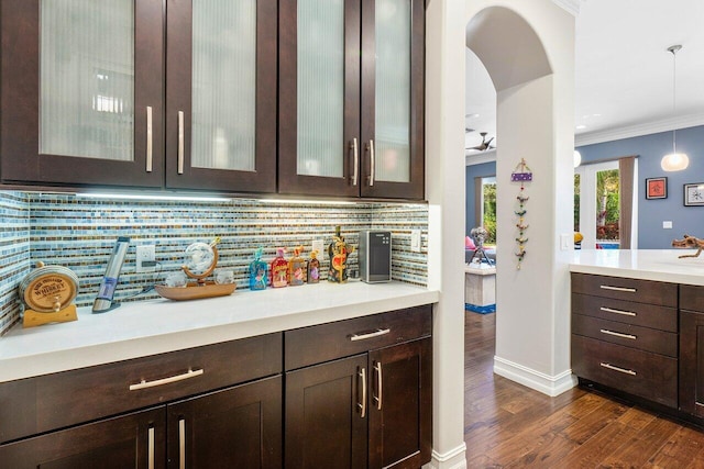 bar featuring pendant lighting, decorative backsplash, dark brown cabinets, and crown molding