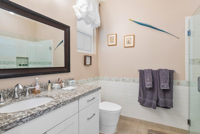 bathroom featuring tile patterned floors, vanity, tile walls, toilet, and a shower with shower door