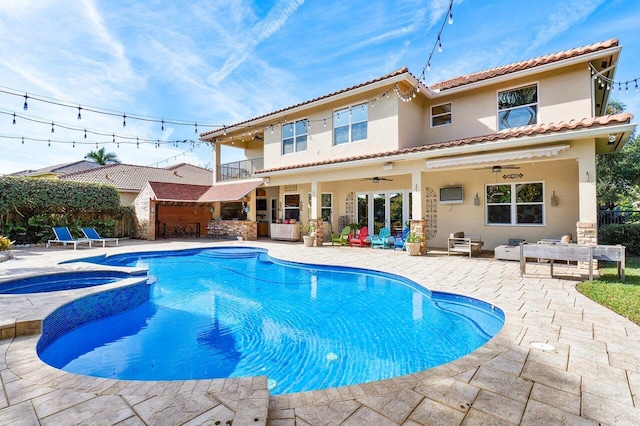 rear view of property featuring a swimming pool with hot tub, a patio area, ceiling fan, and a balcony