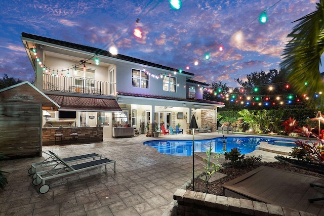 back house at dusk featuring area for grilling, ceiling fan, a balcony, and a patio area