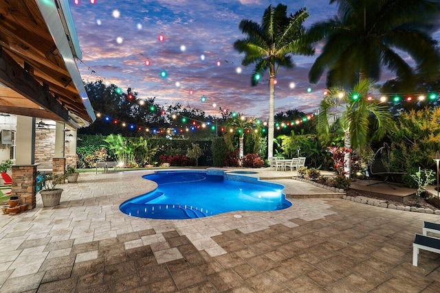 pool at dusk featuring an in ground hot tub and a patio