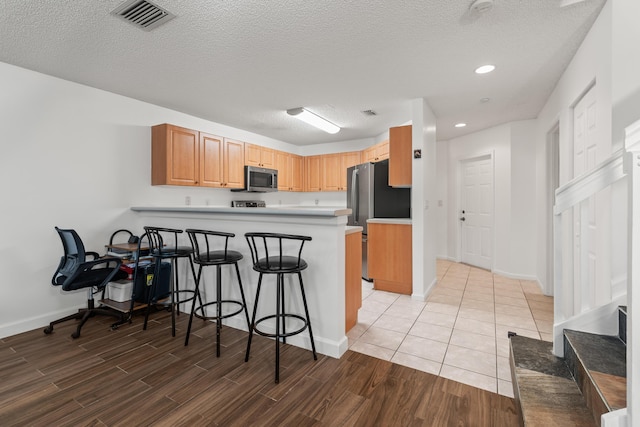 kitchen featuring kitchen peninsula, appliances with stainless steel finishes, a textured ceiling, and a kitchen bar