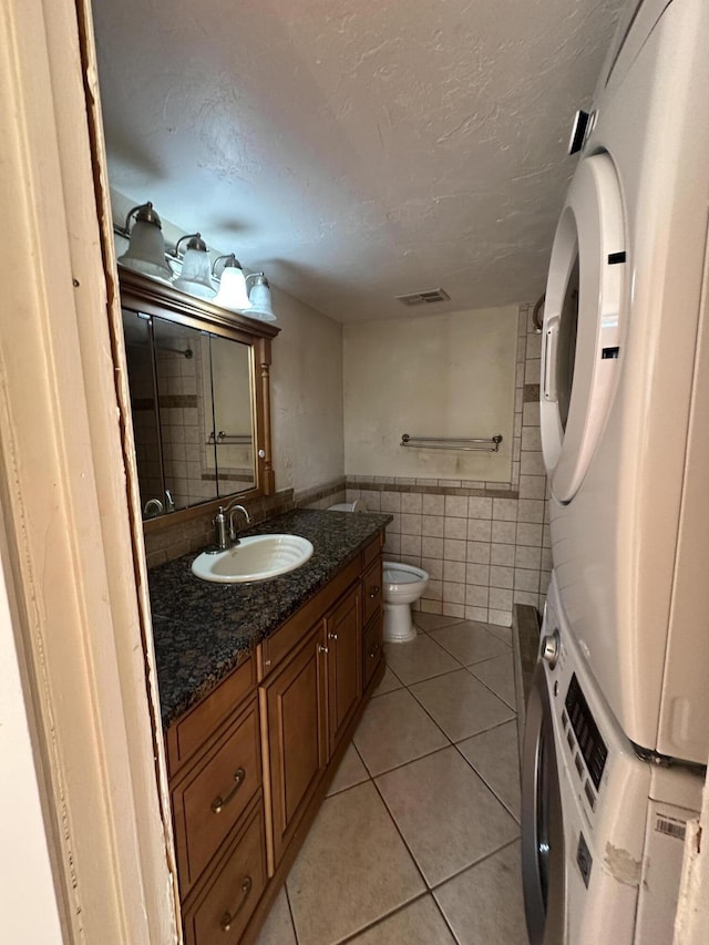 bathroom featuring vanity, tile patterned floors, toilet, walk in shower, and stacked washer / dryer