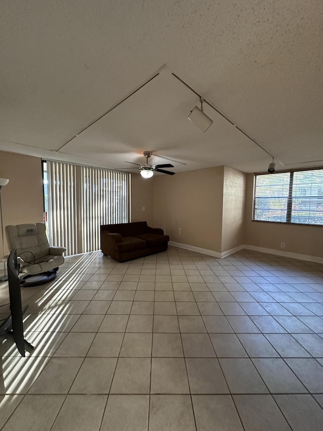 unfurnished living room featuring rail lighting, ceiling fan, light tile patterned floors, and a textured ceiling