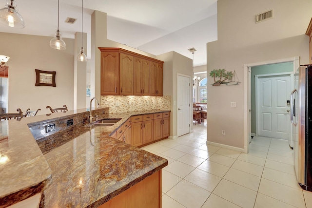 kitchen with light tile patterned floors, decorative light fixtures, dark stone countertops, stainless steel refrigerator, and sink