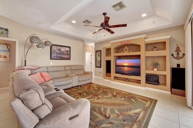 living room featuring ceiling fan, light tile patterned floors, built in shelves, and a tray ceiling