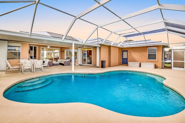 pool at dusk featuring glass enclosure, a patio area, and outdoor lounge area