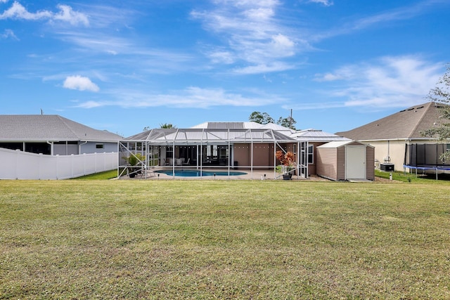 back of property with a lawn, a fenced in pool, a storage unit, and glass enclosure