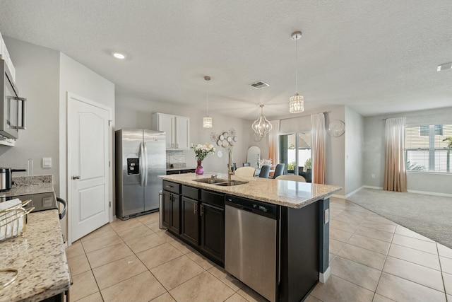 kitchen featuring sink, stainless steel appliances, pendant lighting, light colored carpet, and a kitchen island with sink