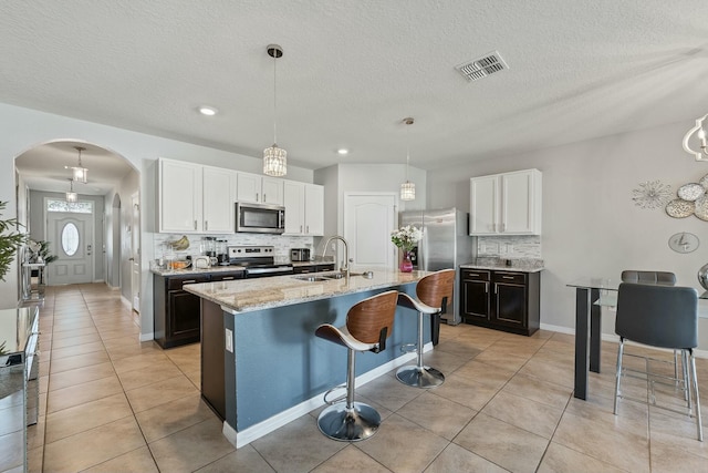 kitchen with white cabinets, hanging light fixtures, sink, an island with sink, and appliances with stainless steel finishes