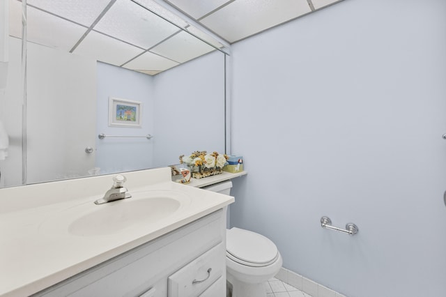 bathroom with tile patterned flooring, vanity, a drop ceiling, and toilet