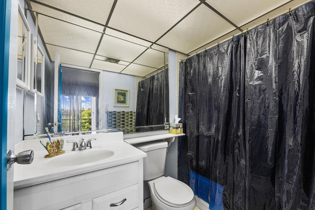 bathroom with a paneled ceiling, vanity, toilet, and walk in shower