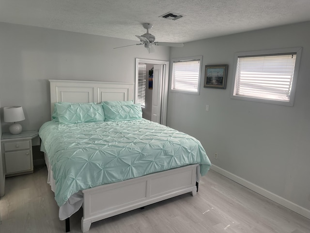 bedroom featuring light wood-type flooring, a textured ceiling, ceiling fan, a spacious closet, and a closet