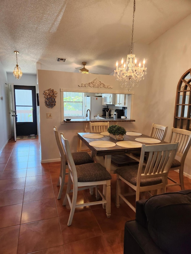 dining space featuring dark tile patterned flooring, ceiling fan with notable chandelier, and a textured ceiling