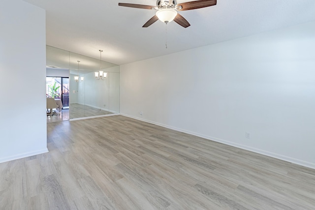 empty room with ceiling fan with notable chandelier and light hardwood / wood-style floors