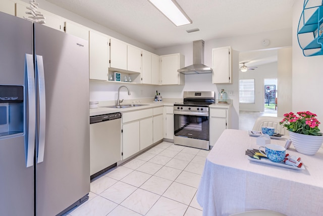 kitchen with wall chimney exhaust hood, sink, ceiling fan, stainless steel appliances, and white cabinets