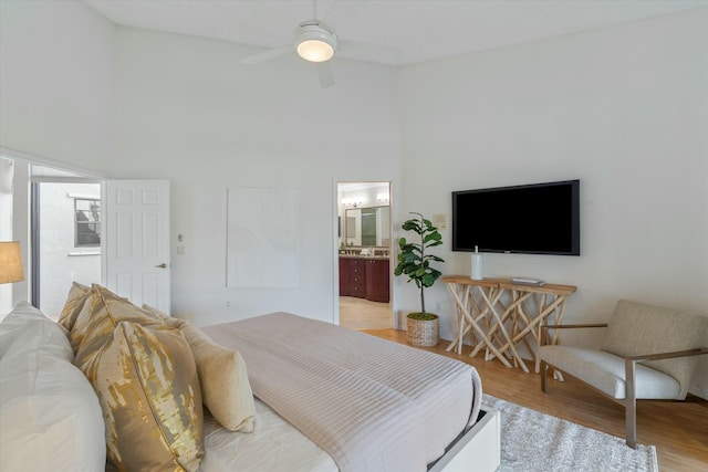 bedroom featuring ceiling fan, light wood-type flooring, connected bathroom, and a towering ceiling