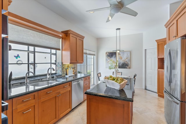 kitchen featuring dark stone counters, sink, appliances with stainless steel finishes, decorative light fixtures, and a kitchen island