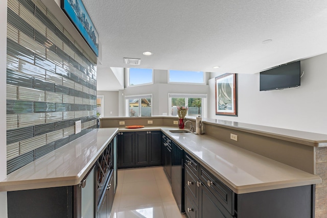 kitchen with sink, a textured ceiling, vaulted ceiling, light tile patterned floors, and kitchen peninsula