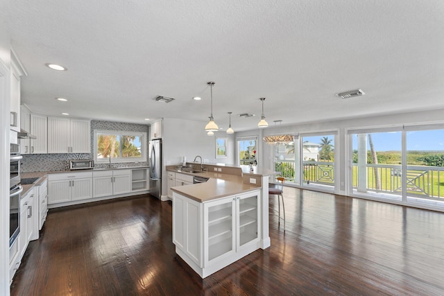 kitchen with stainless steel appliances, white cabinets, pendant lighting, backsplash, and a kitchen island with sink