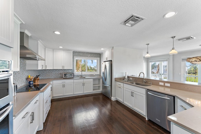 kitchen with stainless steel appliances, sink, white cabinetry, wall chimney range hood, and pendant lighting