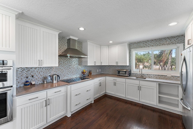 kitchen with a textured ceiling, wall chimney exhaust hood, white cabinets, appliances with stainless steel finishes, and sink