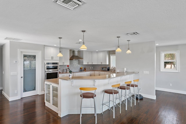 kitchen featuring white cabinetry, decorative light fixtures, backsplash, and wall chimney exhaust hood