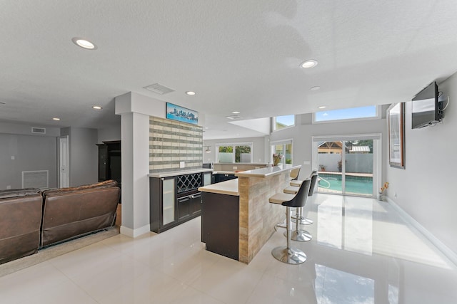 kitchen featuring a textured ceiling, a kitchen breakfast bar, light tile patterned flooring, and kitchen peninsula