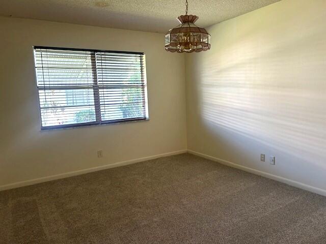 carpeted spare room featuring a chandelier and a textured ceiling