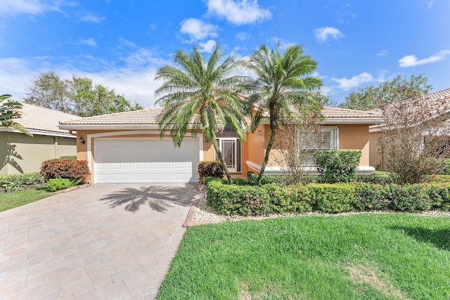 single story home featuring an attached garage, a tile roof, decorative driveway, stucco siding, and a front yard