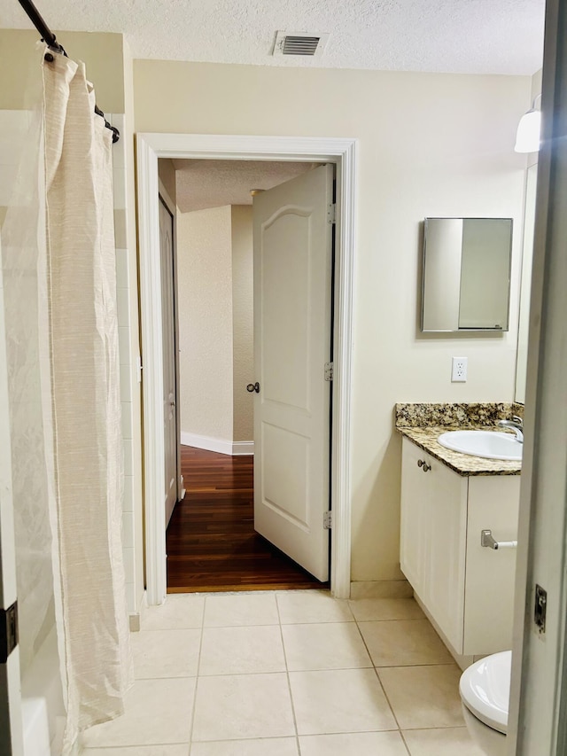 bathroom with tile patterned flooring, vanity, a textured ceiling, and walk in shower