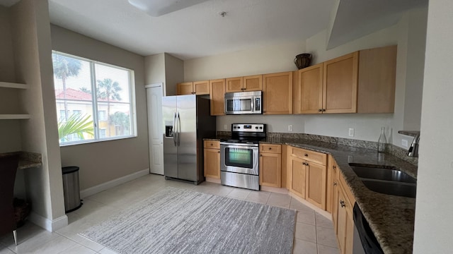 kitchen featuring stainless steel appliances, sink, dark stone counters, and light tile patterned floors